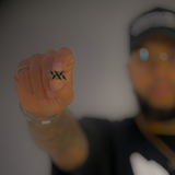 Hand holding the DNA Strand lapel pin in front of a blurred background, featuring the signature IAC Lyfestyle DNA logo.