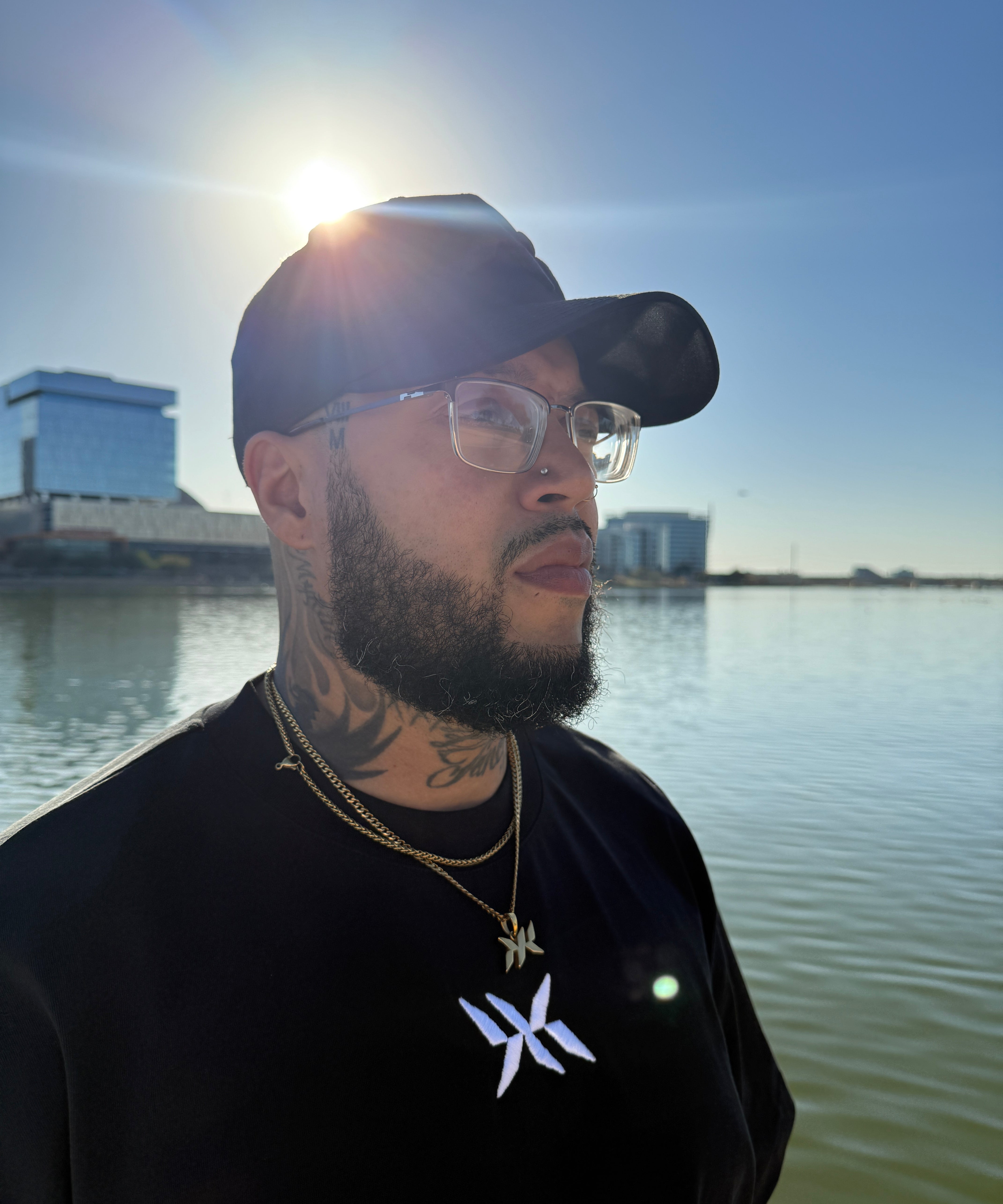 Model wearing IAC Essentials Kit featuring DNA Strand logo tee, snapback hat, and DNA pendant chain by water