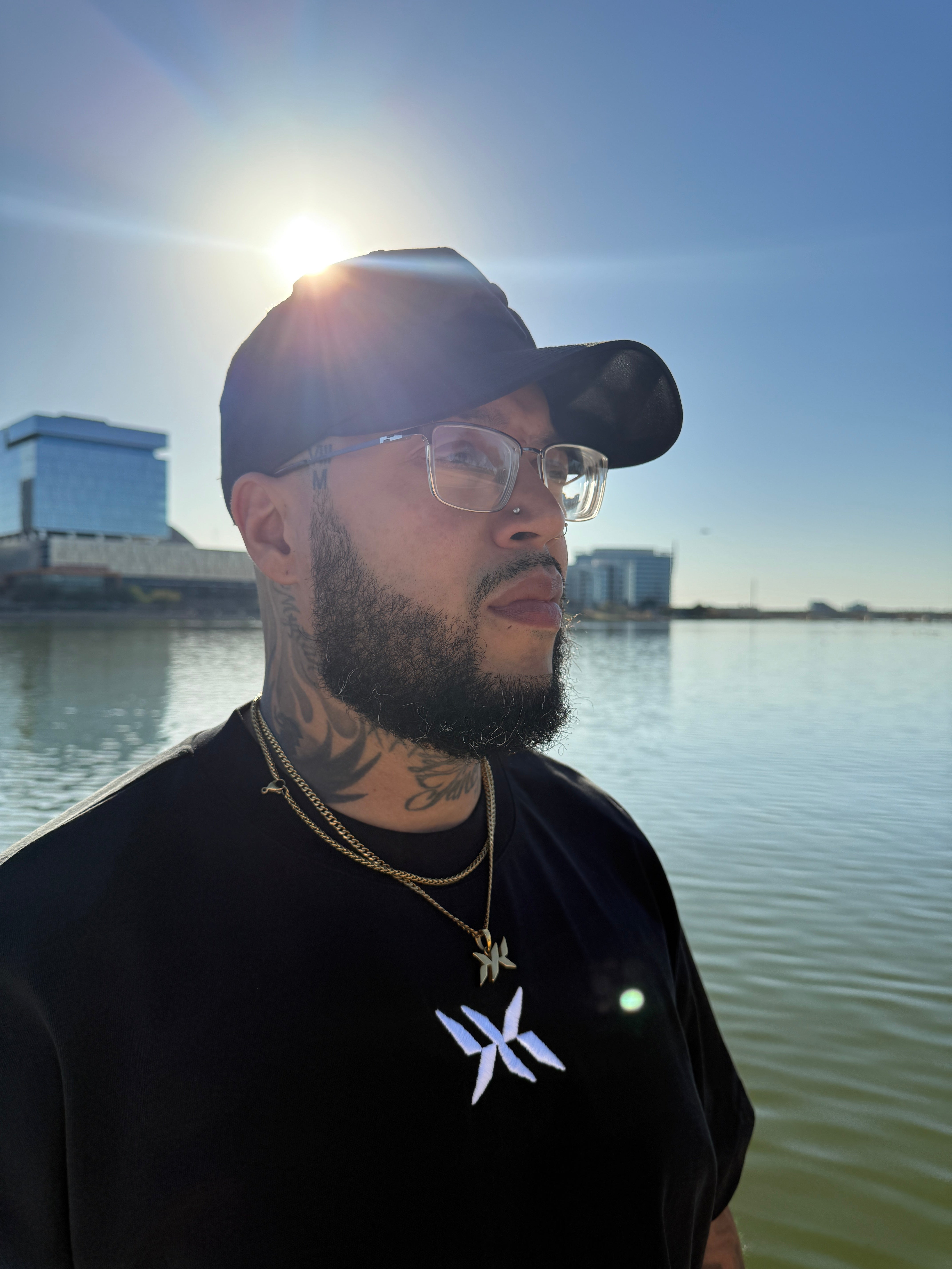 Model wearing IAC Essentials Kit featuring DNA Strand logo tee, snapback hat, and DNA pendant chain by water