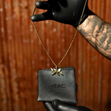 DNA Strand pendant necklace in gold hanging over black IAC leather pouch, held by hand against textured background